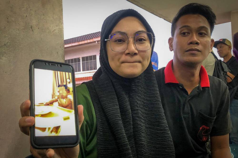 Mother of the victim, Ainol Izzah Raslan, 25 and the father, Nazrul Nizam Mohd Tahar, 29, showing a picture of their baby at the Forensic Unit of Melaka Hospital. Photo by Bernama