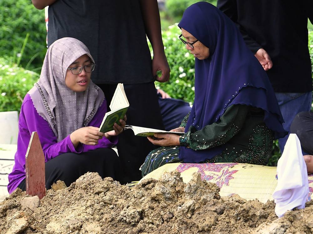 The mother of the late drowning victim, Corporal Muhammad Taufik Sayutin, Jamiah Mansor (right), recites Yassin. - Photo by Bernama