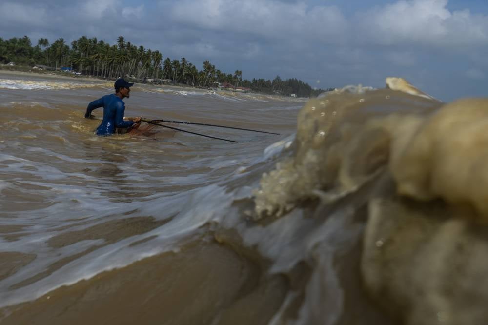 Fishermen brave strong waves crashing along the shoreline to scoop up mullets. - Photo by Bernama