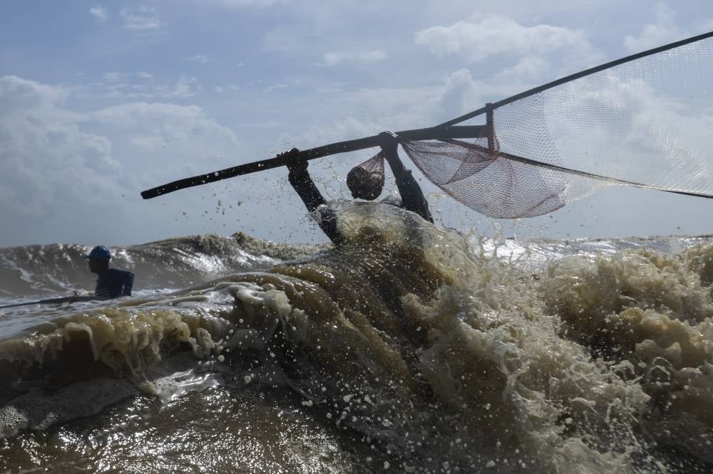Fishermen brave strong waves crashing along the shoreline to scoop up mullets. - Photo by Bernama