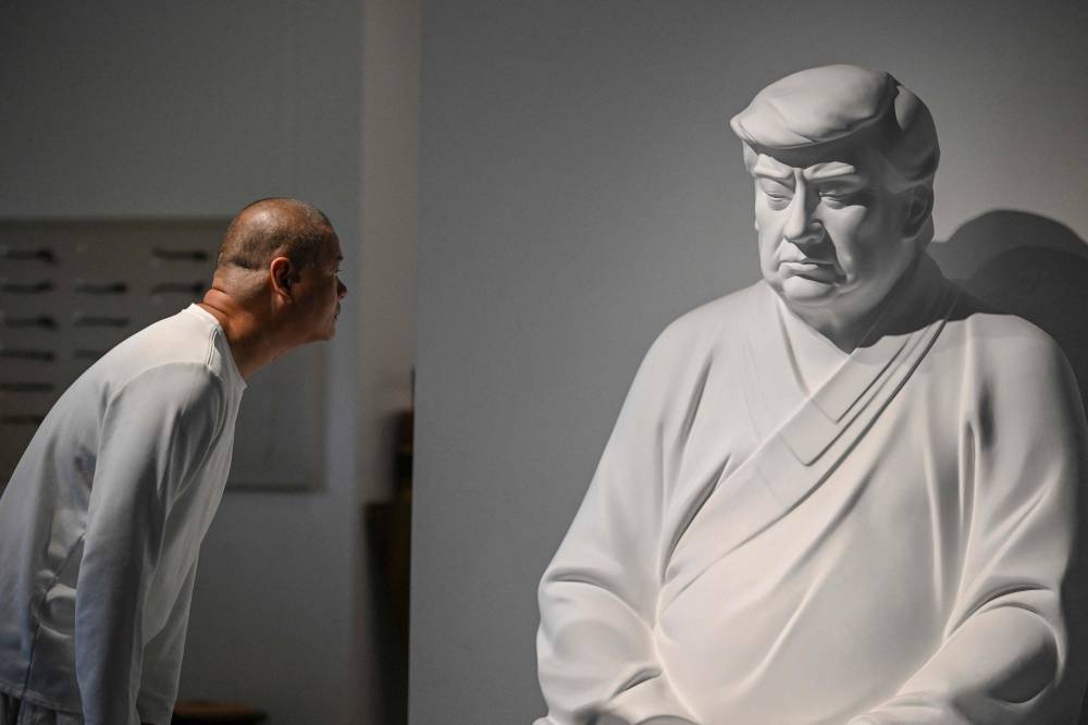 This photo taken on December 9, 2024 shows artist Hong Jinshi looking at a sculpture of US president-elect Donald Trump in a pose evoking the Buddha at his workshop in Xiamen, in southeastern China's Fujian province. - Photo by AFP