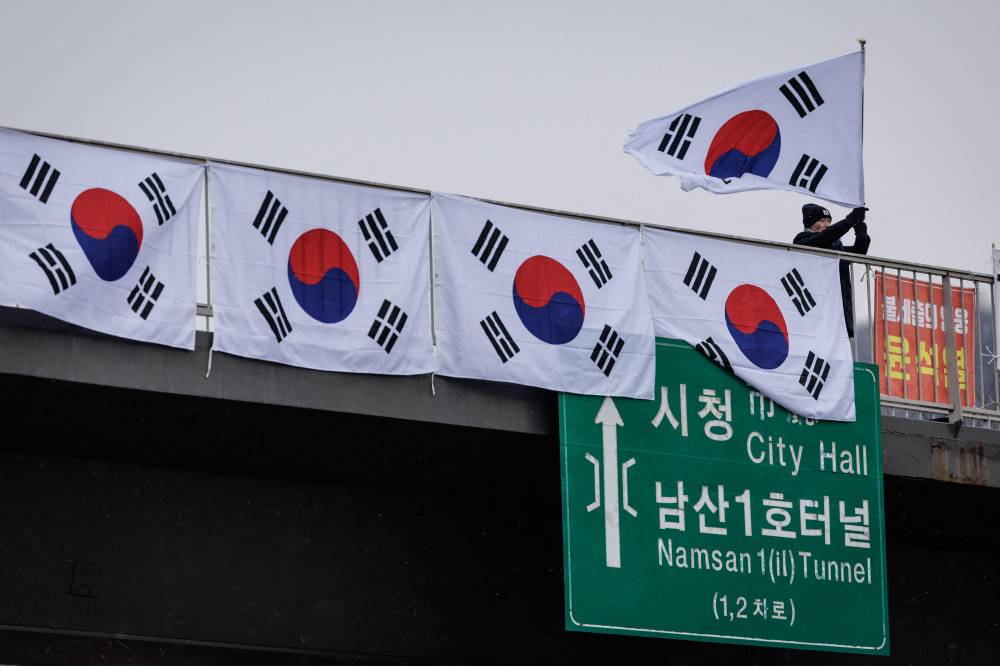 A supporter of impeached South Korean President Yoon Suk Yeol waves the national flag from a pedestrian bridge near the presidential residence before sunrise in Seoul on January 13, 2025. (Photo by YASUYOSHI CHIBA / AFP)