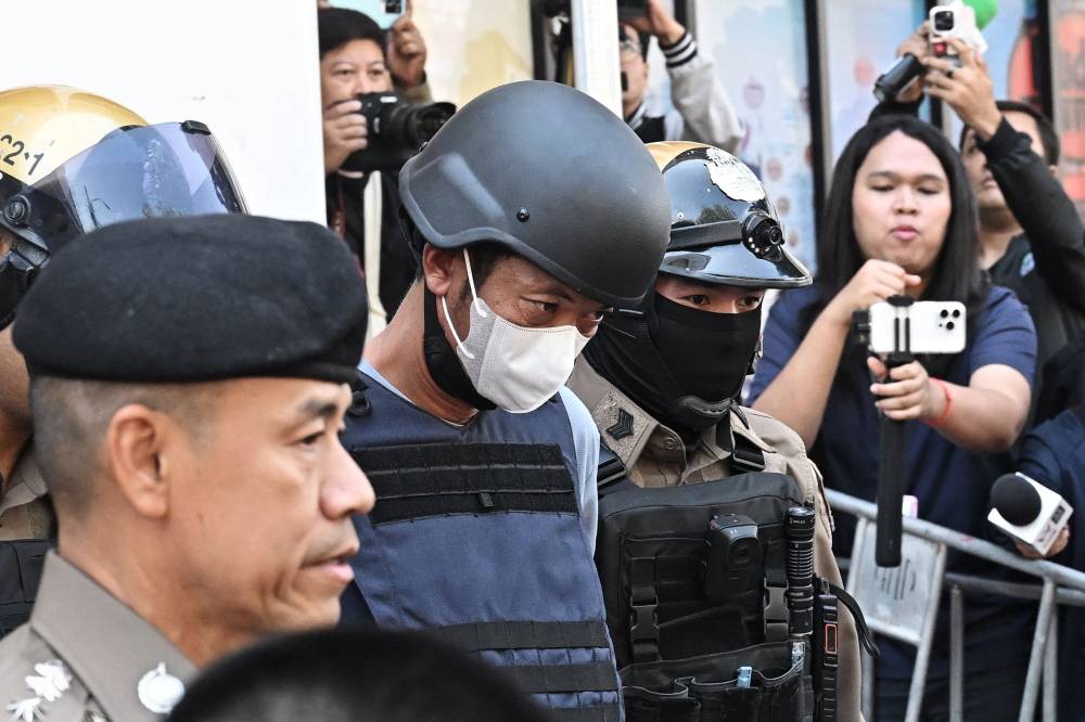 Thai national Ekalak Paenoi (C), a suspect in the alleged killing of former lawmaker of the dissolved Cambodia National Rescue Party (CNRP) Lim Kimya, is escorted into a police van to transport him to the Criminal Court from Chana Songkram Police Station in Bangkok on January 13, 2025. (Photo by Lillian SUWANRUMPHA / AFP)
