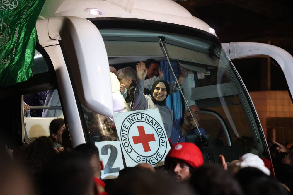 Palestinian prisoners released from jail by Israel under a truce with Hamas in Gaza wave to the crowd from inside a Red Cross bus upon their arrival. Photo by Zain Jaafar/AFP