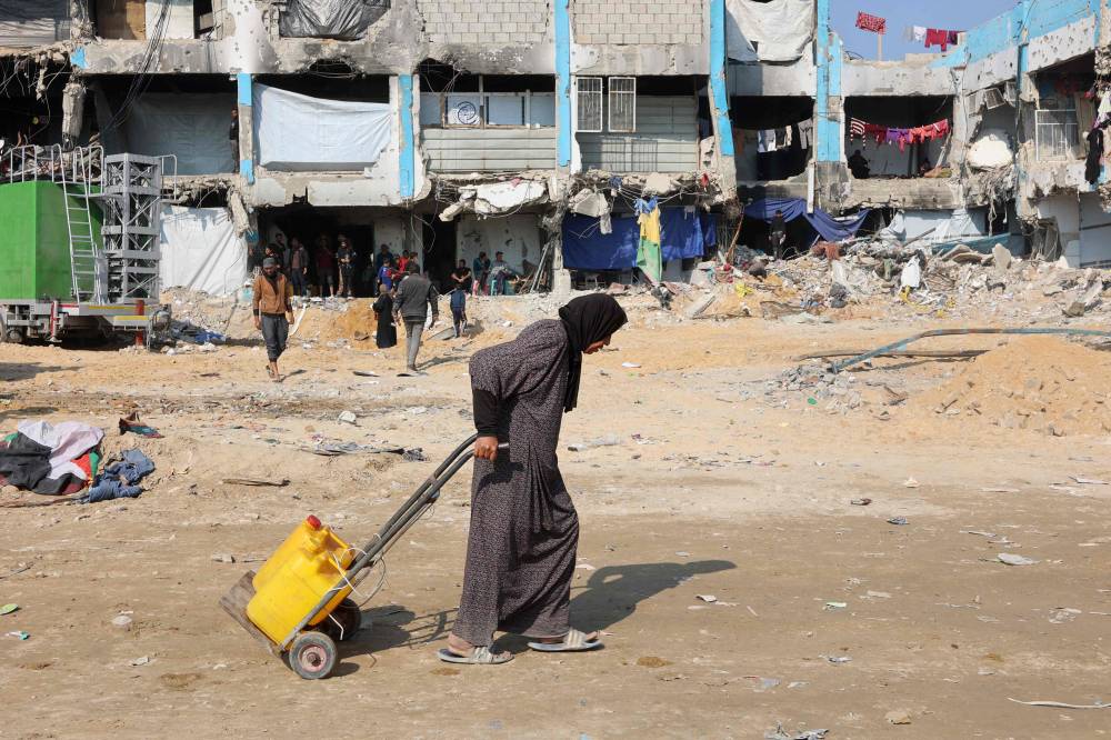 A Palestinian woman pulls a trolley with water cans in Jabalia in the northern Gaza Strip. Photo by Omar Al-Qattaa/AFP