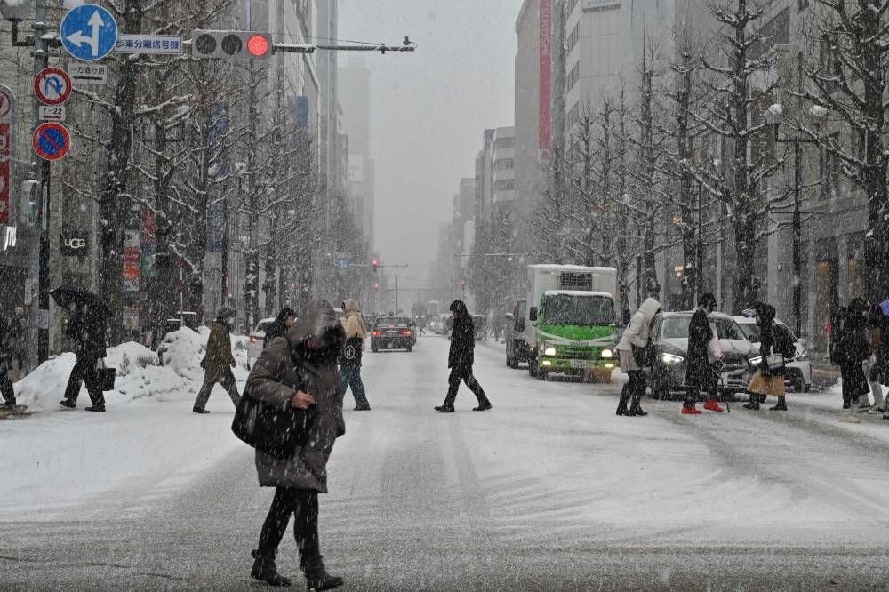 This photo taken on February 18, 2025 shows pedestrians crossing the street in the snow in central Sapporo, Hokkaido prefecture. (Photo by Richard A. Brooks / AFP)