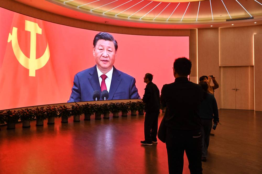 A screen shows images of China's President Xi Jinping. (Photo by HECTOR RETAMAL / AFP)