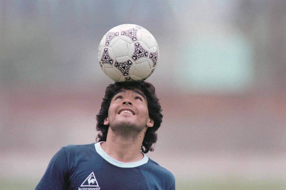 Argentine star Diego Maradona, wearing a diamond earring, balances a soccer ball on his head as he walks off the practice field following the national selection's 22 May 1986 practice session in Mexico City. (Photo by JORGE DURAN / AFP)