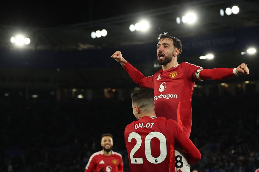 Manchester United's Portuguese midfielder #08 Bruno Fernandes leaps into the arms of Manchester United's Portuguese defender #20 Diogo Dalot as he celebrates scoring their third goal during the English Premier League football match between Leicester City and Manchester United at King Power Stadium in Leicester, central England on March 16, 2025. (Photo by Adrian Dennis / AFP) / RESTRICTED TO EDITORIAL USE. No use with unauthorized audio, video, data, fixture lists, club/league logos or 'live' services. Online in-match use limited to 120 images. An additional 40 images may be used in extra time. No video emulation. Social media in-match use limited to 120 images. An additional 40 images may be used in extra time. No use in betting publications, games or single club/league/player publications. /