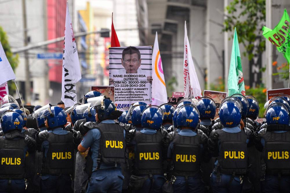 Protesters carrying a placard showing former president Rodrigo Duterte are blocked by anti-riot policemen near Malacanang palace in Manila on March 17, 2025. (Photo by TED ALJIBE / AFP)