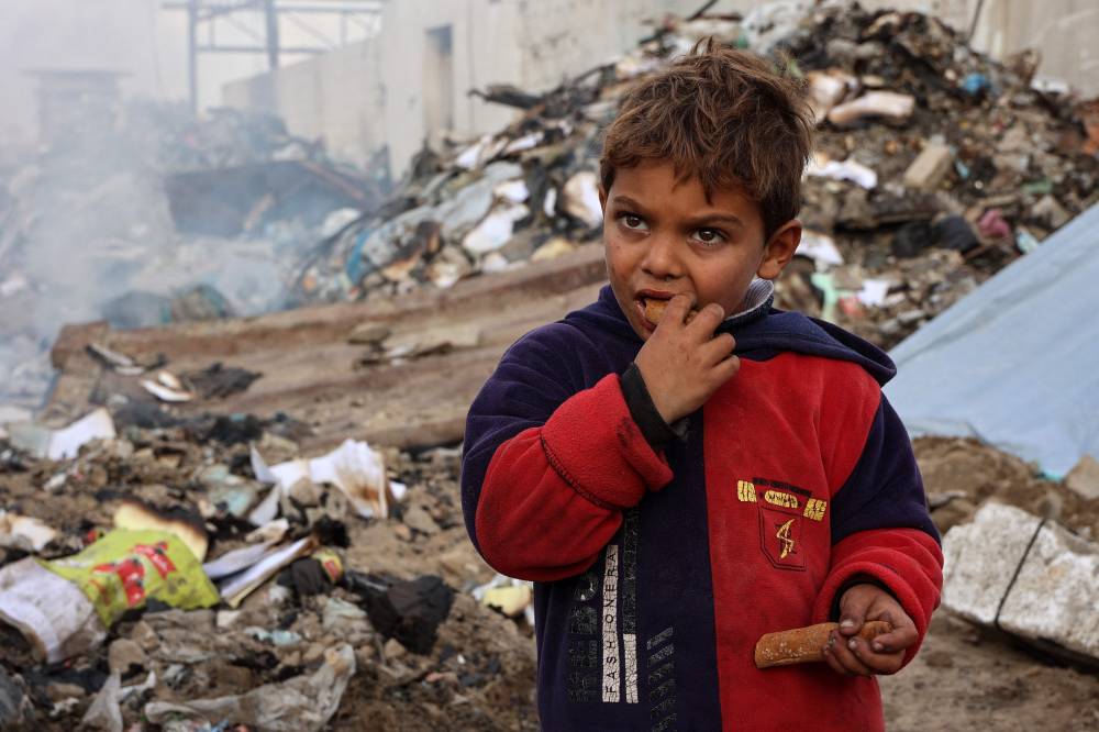 A boy looks on as he eats at a camp sheltering displaced Palestinians set up at a landfil in the Yarmuk area in Gaza City on March 20, 2025. (Photo by Omar AL-QATTAA/AFP)