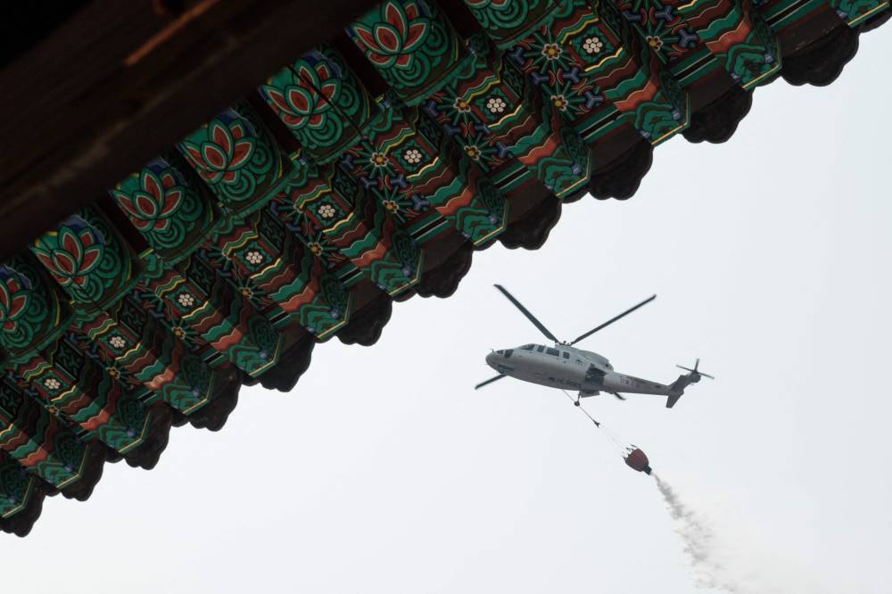 A helicopter drops water as they prepare for the possibility of a wildfire advancing towards Gounsa Temple in Uiseong on March 25, 2025. (Photo by YASUYOSHI CHIBA / AFP)