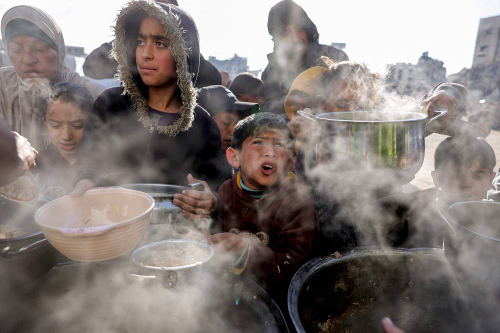 Children hold out empty pots as they queue for charity meals handed out from a kitchen during the Muslim holy fasting month of Ramadan, in Gaza City on March 22, 2025. (Photo by BASHAR TALEB / AFP)