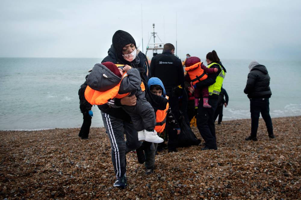 A migrant carries her children after being helped ashore from a RNLI (Royal National Lifeboat Institution) lifeboat at a beach in Dungeness, on the south-east coast of England, on November 24, 2021, after being rescued while crossing the English Channel. (Photo by Ben STANSALL / AFP)
