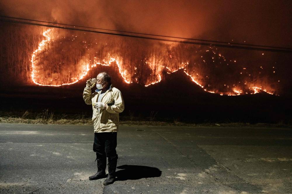 A man talks to his son on the phone under a streetlight on the road in front of his home as wildfires burn in Uiseong, South Korea, on March 24, 2025. (Photo by YASUYOSHI CHIBA / AFP)