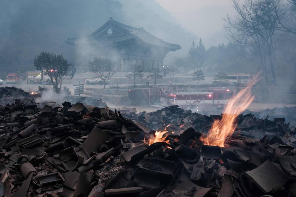 Embers remain among the debris after most of the buildings were burned to the ground in a wildfire at Gounsa Temple in Uiseong on March 26, 2025. (Photo by YASUYOSHI CHIBA / AFP)