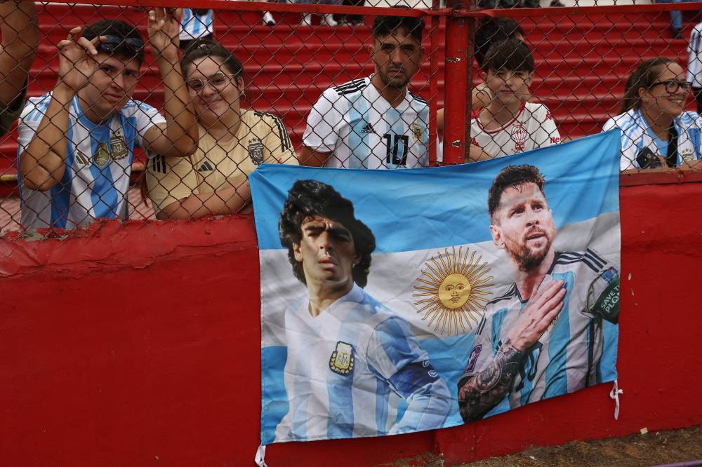 Argentina's national football fans with a flag with the picture of late Argentine football legend Diego Maradona and Forward Lionel Messi attend a training session with the U20 national team at the Tomas Adolfo Duco Stadium in Buenos Aires, on March 22, 2025, in support of the city of Bahia Blanca, hit by a storm that left 16 people dead. Argentina will face Brazil on March 25 in the South American qualifiers for the FIFA 2026 World Cup. (Photo by ALEJANDRO PAGNI/AFP)