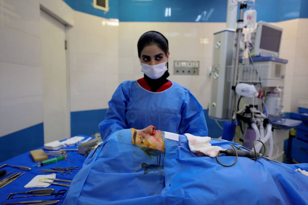 A member of the surgical team stands next to a patient during a nose operation at a private clinic in Tehran, on March 4, 2025. (Photo by ATTA KENARE / AFP)