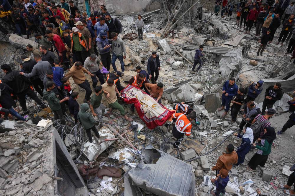 People watch as Palestinian rescuers transport a body from the rubble after an Israeli strike on the Manoun family home in Jabalia in the northern Gaza Strip on April 13, 2025. - (Photo by BASHAR TALEB / AFP)