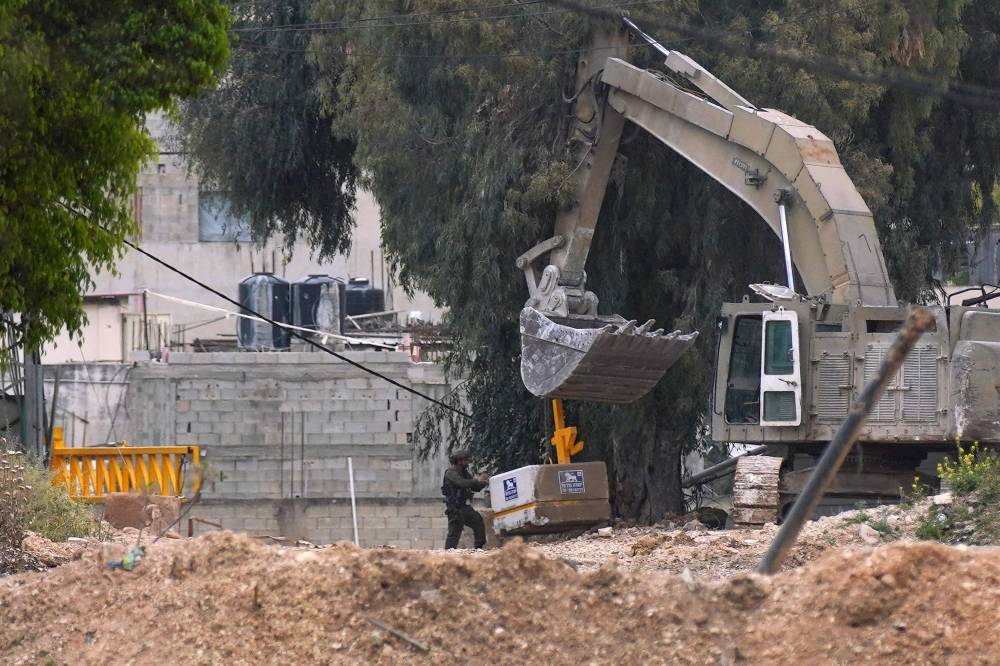 An Israeli soldier pushes a cement block as the army uses an excavator to install an iron gate at one of the entrances of the Jenin refugee camp in the occupied-West Bank on April 23, 2025. - (Photo by Mohammed Mansour / AFP)