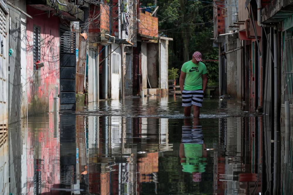 A man walks through flooded waters at Jardim Pantanal neighborhood in Sao Paulo on February 5, 2025. Floods, massive power outages, fallen trees, kilometre-long traffic jams: every time there is a storm, chaos stalks one of the largest cities in the world and the economic heart of Brazil. Associated with climate change, the storms have transformed the lives of the 12 million inhabitants of Sao Paulo, a city that has always boasted of functioning better than others such as Rio de Janeiro and whose services and infrastructure have made it a mecca for large companies. (Photo by Miguel SCHINCARIOL / AFP)