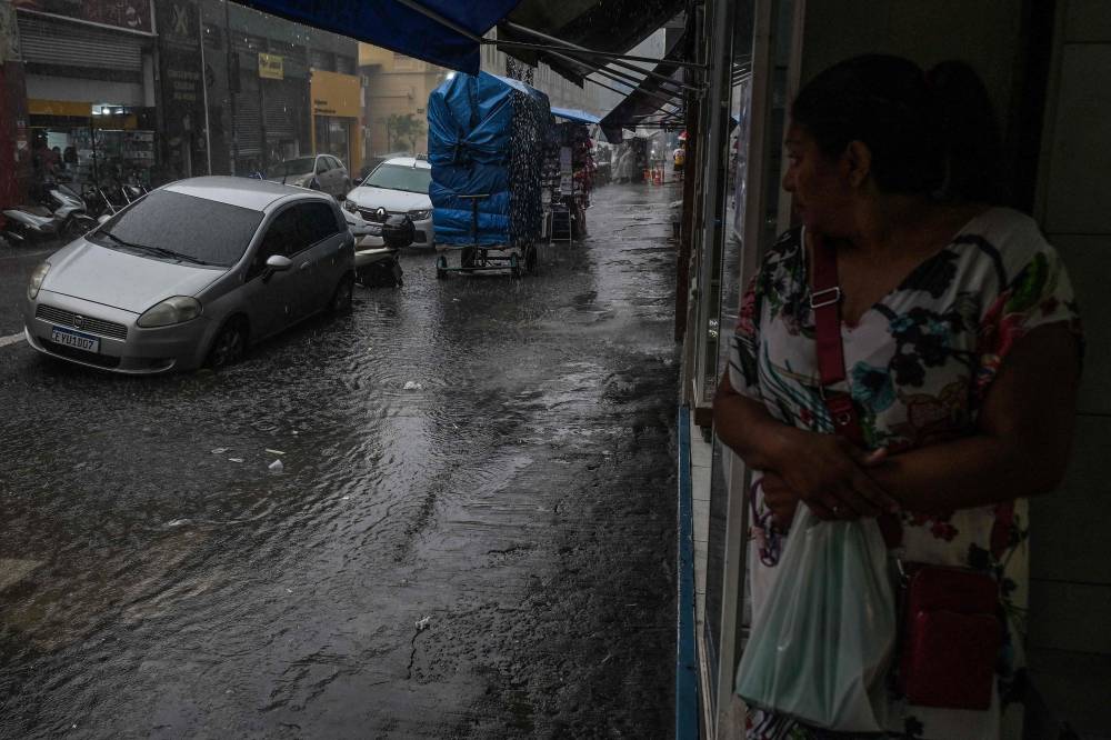A woman takes shelter from the rain in a store during heavy rains in downtown Sao Paulo, Brazil, on February 18, 2025. Floods, massive power outages, fallen trees, kilometre-long traffic jams: every time there is a storm, chaos stalks one of the largest cities in the world and the economic heart of Brazil. Associated with climate change, the storms have transformed the lives of the 12 million inhabitants of Sao Paulo, a city that has always boasted of functioning better than others such as Rio de Janeiro and whose services and infrastructure have made it a mecca for large companies. (Photo by Nelson ALMEIDA / AFP)