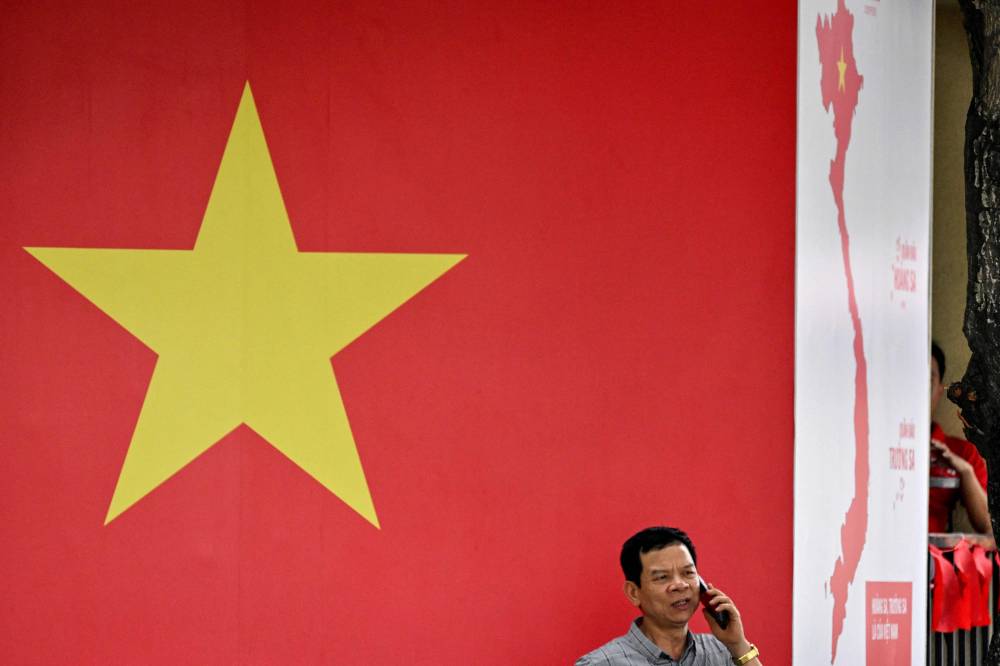 A man uses his phone in front of a flag and map of Vietnam in Ho Chi Minh City on April 29, 2025, ahead of the celebrations on April 30 to mark 50 years since the communists of North Vietnam defeated the US-backed South in a victory that ended the Vietnam War. (Photo by Nhac NGUYEN / AFP)