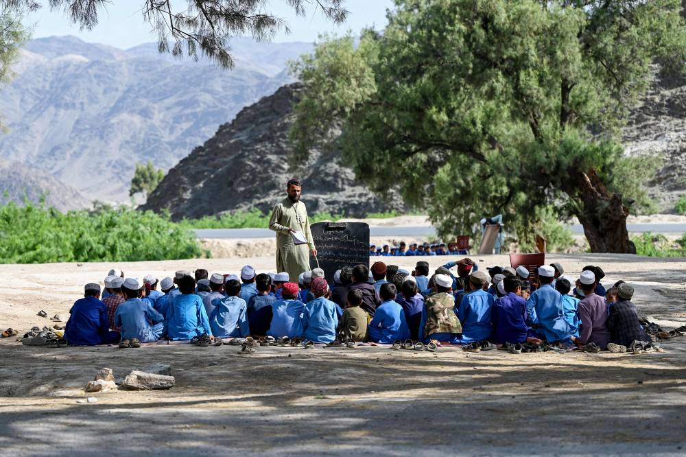 Afghan boys attend a class at an open air school next to a cemetery in the Mohmand Dara district of Nangarhar province on April 20, 2025. Since the start of the school year in March, Afghan boys have been required to wear new uniforms of turbans and long tunics, following an order to adopt outfits reflecting Taliban rule. (Photo by Wakil KOHSAR/AFP)