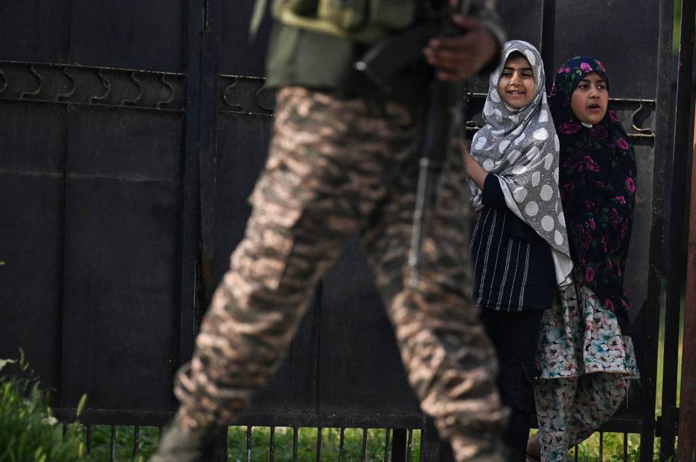 An Indian security personnel (L) stands guard as people watch on in Wuyan near Indian-administered Kashmir's main city of Srinagar on May 7, 2025. (Photo by TAUSEEF MUSTAFA/AFP)
