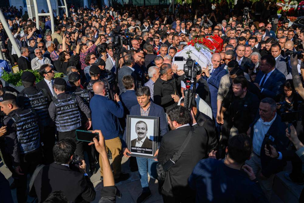 A man holds a portrait of MP's of pro-Kurdish Equality and Democracy (DEM) Party Sirri Sureyya Onder as mourners carry the coffin covered by red carnations at Barbaros Hayrettin Mosque in Istanbul on May 4, 2025. MP's of pro-Kurdish Equality and Democracy (DEM) Party Sirri Sureyya Onder died aged 62, an Istanbul hospital said on May 3, 2025, after undergoing heart surgery on April 15 two and a half weeks after suffering a cardiac arrest on 15 April. (Photo by Yasin AKGUL / AFP)