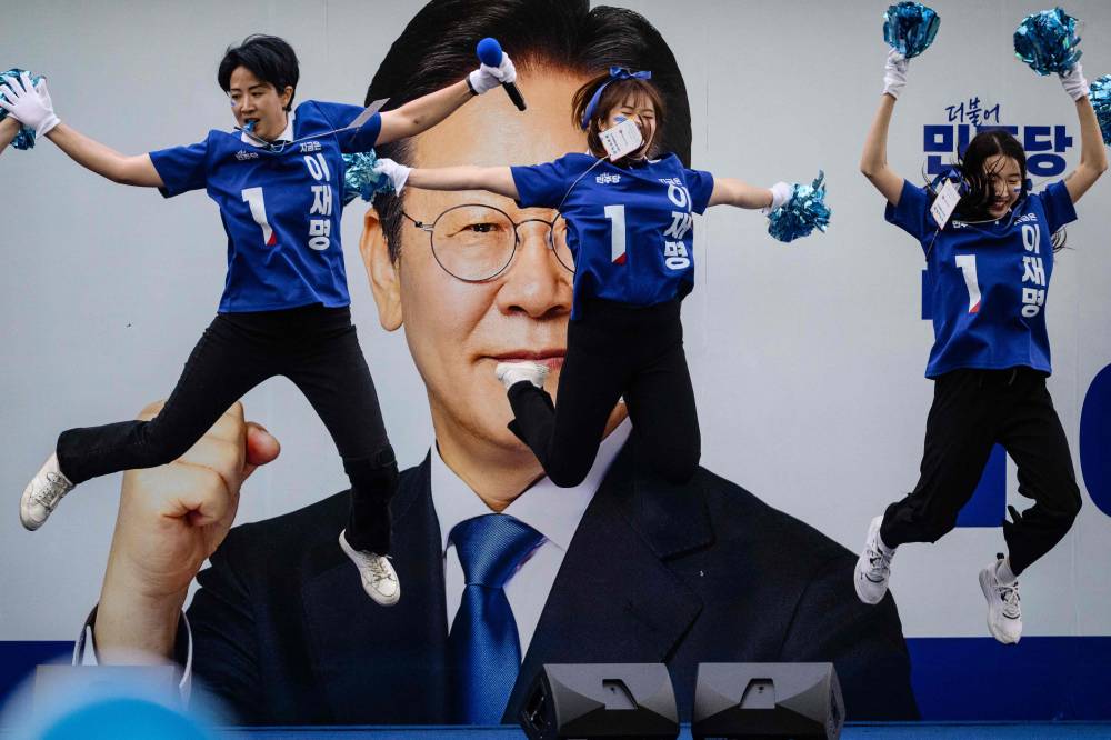 TOPSHOT - Supporters of South Korean presidential candidate, Lee Jae-myung (pictured on poster) of the Democratic Party dance before a televised presidential debate for the forthcoming June 3 presidential election on a road outside the SBS studio in Seoul on May 18, 2025. (Photo by ANTHONY WALLACE / AFP)
