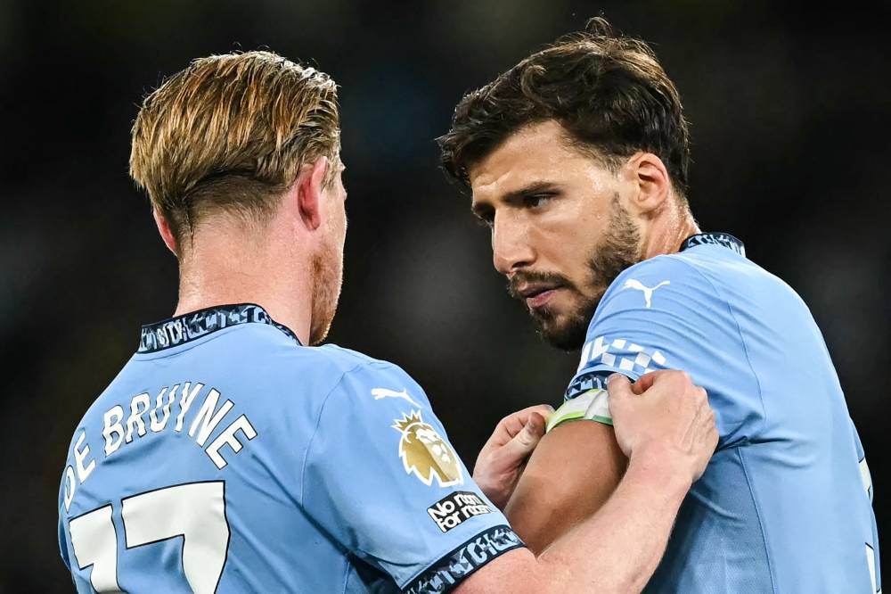 Manchester City's Belgian midfielder #17 Kevin De Bruyne (L) gives his captain arm band to Manchester City's Portuguese defender Ruben Dias as he leaves the pitch at the end of his last match with Manchester City during the English Premier League football match between Manchester City and Bournemouth at the Etihad Stadium in Manchester, north west England, on May 20, 2025. (Photo by Paul ELLIS/AFP)