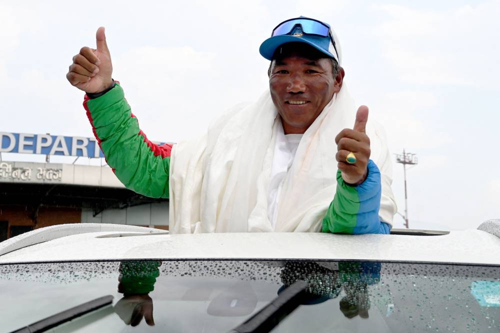 Nepali mountaineer Kami Rita Sherpa, who broke his own record after scaling Mount Everest for the 30th time, gestures to the crowd upon his arrival at the Tribhuvan International airport in Kathmandu on May 24, 2024.(Photo by Prakash MATHEMA / AFP)