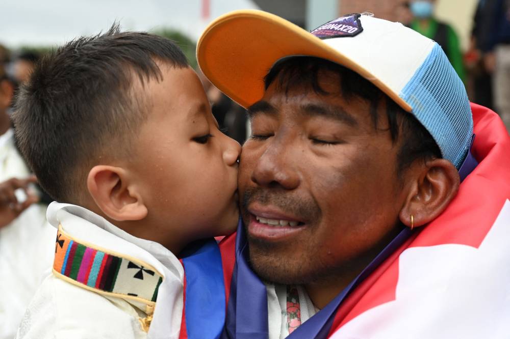 Nepali climber Tashi Gyalzen Sherpa embraces his son upon his arrival at Tribhuvan International Airport in Kathmandu on May 27, 2025, after he made a record-breaking four summits of Everest in fifteen days. Nepal has issued more than 1,100 permits for mountaineers this season, including 458 for Everest, earning more than $5 million in royalties. The country is home to eight of the world's 10 highest peaks and welcomes hundreds of adventurers each spring, when temperatures are warmer and winds typically calmer. (Photo by PRAKASH MATHEMA / AFP)