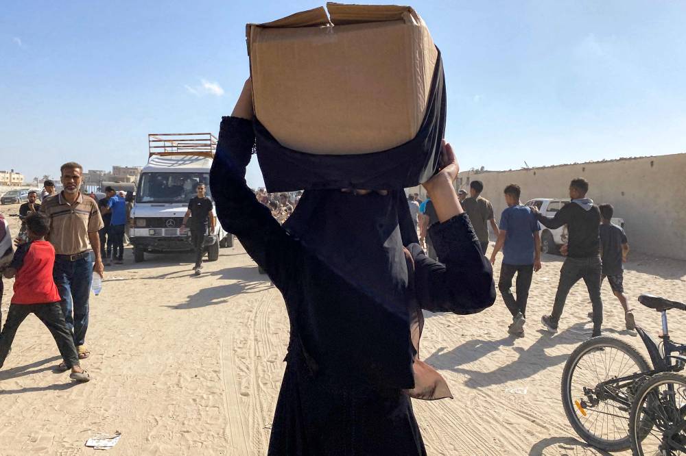 A woman walks carrying a package atop her head as she and other displaced Palestinians receive food packages from a US-backed foundation pledging to distribute humanitarian aid in western Rafah in the southern Gaza Strip on May 27, 2025. - (Photo by AFP)