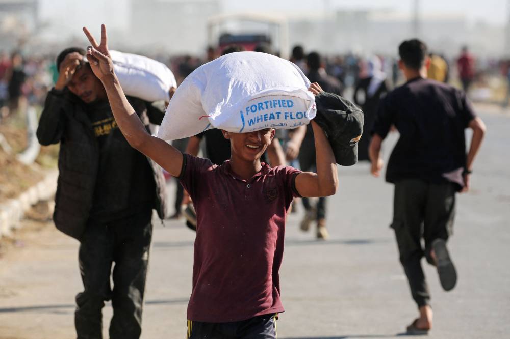 Displaced Palestinians ferry bags of food aid after storming a World Food Programme warehouse in Deir el-Balah in the central Gaza Strip on May 28, 2025. - (Photo by EYAD BABA / AFP)