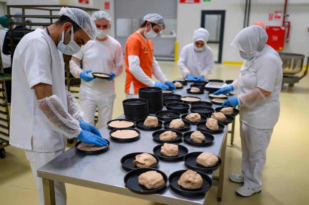 Employees of Halk Ekmek (Public bread, in Turkish), a municipal bakery aiming to provide low cost bread in Eskisehir, mix and cut dough in order to make Kulluoba breads, a reproduction of a 5,000 years old bread unearthed in an archeological excavation, in Eskisehir province, in central Turkey, on May 23, 2025. A 5,000-year-old loaf of bread was discovered in September 2024 by archaeologists in Eskisehir province, central Turkey. Since May 22, the municipality has been reproducing it using the original recipe and plans to revive the cultivation of ancient wheat, which is better suited to drought. (Photo by Yasin AKGUL / AFP)