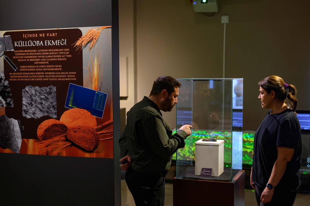 Archeologists Murat Turkteki (L) and Deniz Sari look at Kulluoba bread, a 5,000 years old bread unearthed in an archeological excavation in Eskisehir province, in central Turkey, and exhibitied at Eskisehir ETI archeology museum, on May 23, 2025. A 5,000-year-old loaf of bread was discovered in September 2024 by archaeologists in Eskisehir province, central Turkey. Since May 22, the municipality has been reproducing it using the original recipe and plans to revive the cultivation of ancient wheat, which is better suited to drought. (Photo by Yasin AKGUL / AFP)