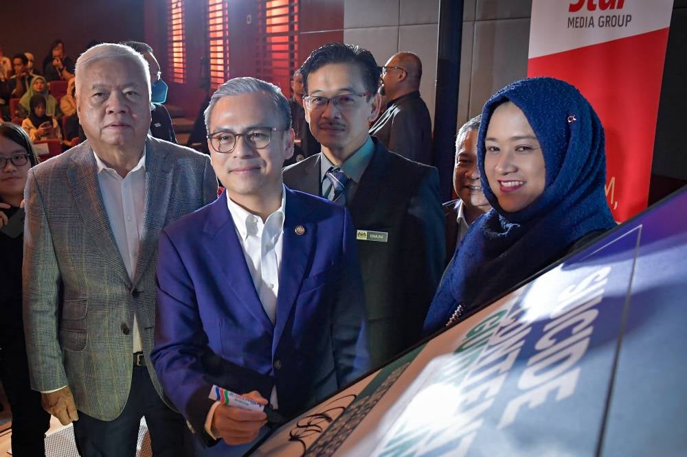 Communications Minister Datuk Fahmi Fadzil signs a report at the launch of the Suicide Content Guidelines at an event today.
