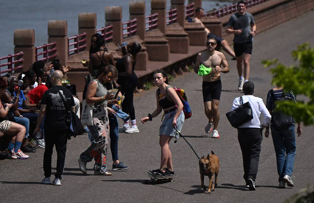 A person skateboards with a dog as people exercise and enjoy the sunshine in Battersea Park, south west London on May 31, 2025. (Photo by JUSTIN TALLIS / AFP)