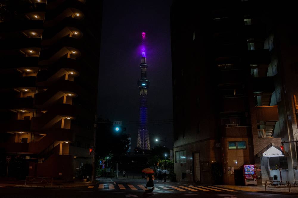 A pedestrian walks across the street as the Tokyo Skytree (C) is seen lit up at the Asakusa district of Tokyo during evening hour on May 30, 2025. (Photo by Philip FONG / AFP)