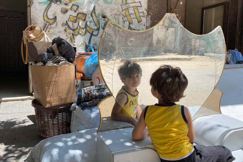 A boy looks in his reflection through a mirror as people pack their belongings to flee from Khan Yunis westwards to al-Mawasi in the southern Gaza Strip on June 3, 2025. - (Photo by AFP)