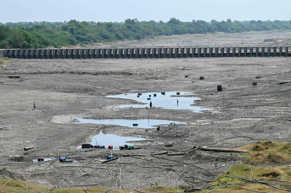 In this photograph taken on May 4, 2025, people walk across the dried-up Godavari river in Beed district in India's Maharashtra state. Farmer suicides have a long history in India, where many are one crop failure away from disaster, but extreme weather caused by climate change is adding fresh pressure. (Photo by Indranil MUKHERJEE/AFP)