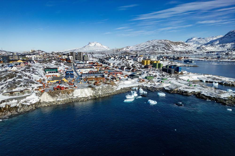 This aerial view shows icebergs floating in the waters beaten down by the sun with buildings in the background off Nuuk, Greenland, on March 11, 2025, on the day of Greenland, the autonomous Danish territory, legislative elections. French President Emmanuel Macron will pay an official visit to Greenland on June 15, 2025, to show his support for this autonomous territory of Denmark coveted by US President Donald Trump, the Elysee Palace announced on June 7, 2025. (Photo by Odd ANDERSEN / AFP)