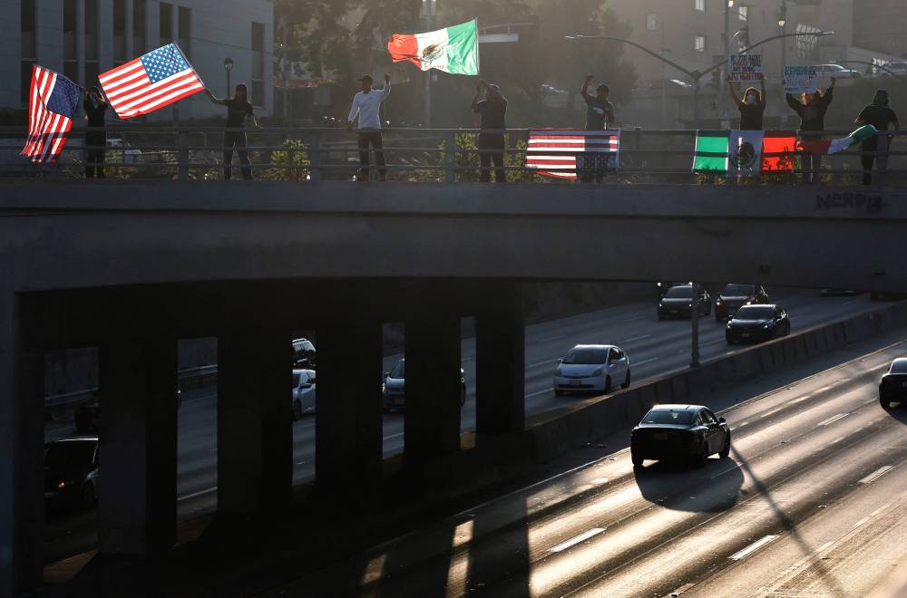 Demonstrators wave American flags and a Mexican flag above the 101 freeway as protests against ICE immigration raids continue in the city on June 11, 2025 in Los Angeles, California. (Photo by MARIO TAMA / GETTY IMAGES NORTH AMERICA / Getty Images via AFP)