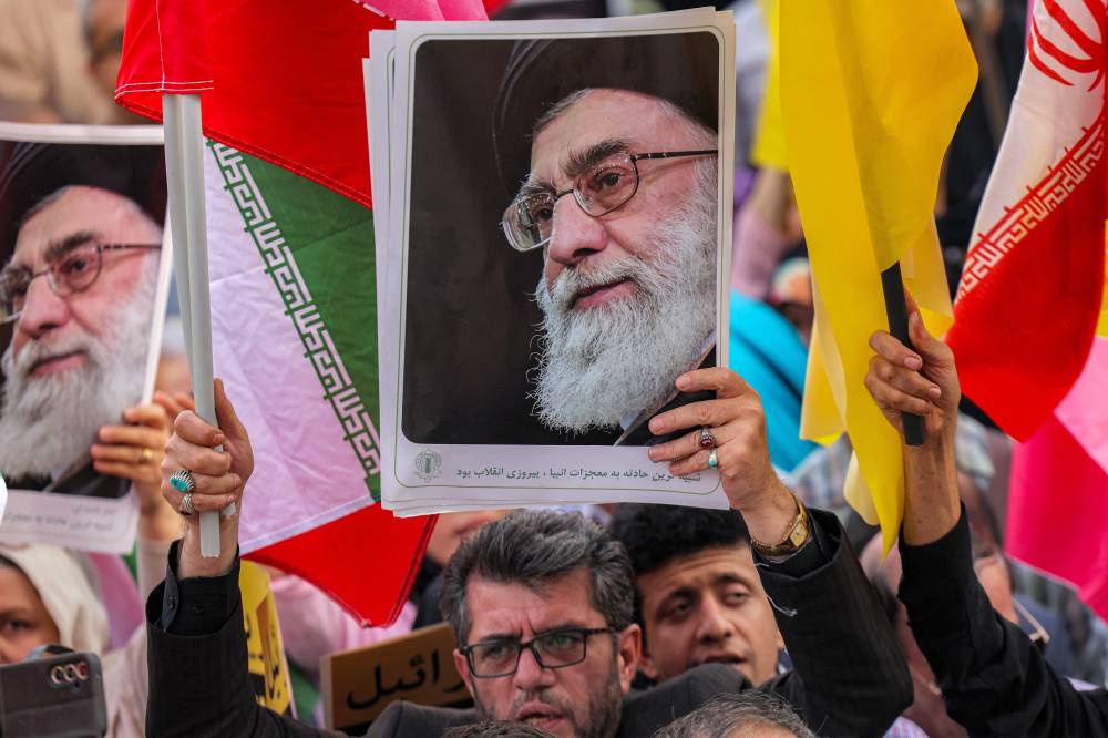 A demonstrator holds a picture of Iran's Supreme Leader Ayatollah Ali Khamenei while gathering with others during a rally in solidarity with the government against Israel's attacks on Iran and to mark Eid al-Ghadir, when according to Shiite Muslim belief the Islamic prophet Mohamed designated his nephew and companion Ali ibn Abi Talib as his successor, at Enghelab (Revolution) Square in Tehran on June 14, 2025. (Photo by ATTA KENARE / AFP)