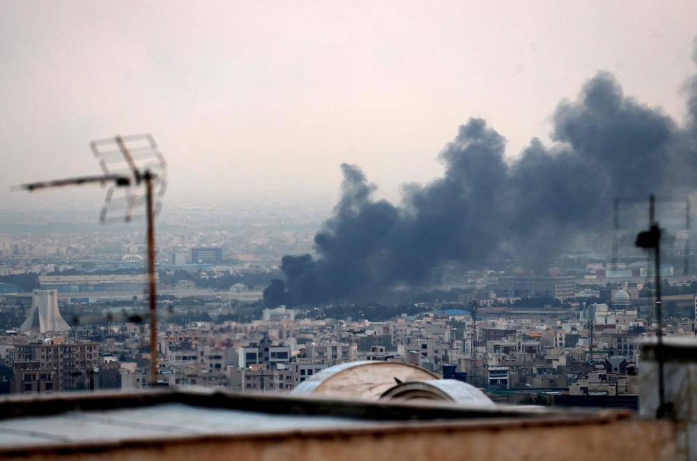 Smoke billows from an explosion near the Azadi Tower (L) in Tehran on June 16, 2025. The Islamic Republic of Iran Broadcasting building was struck in an Israeli attack on June 16, cutting live coverage immediately. - (Photo by ATTA KENARE / AFP)