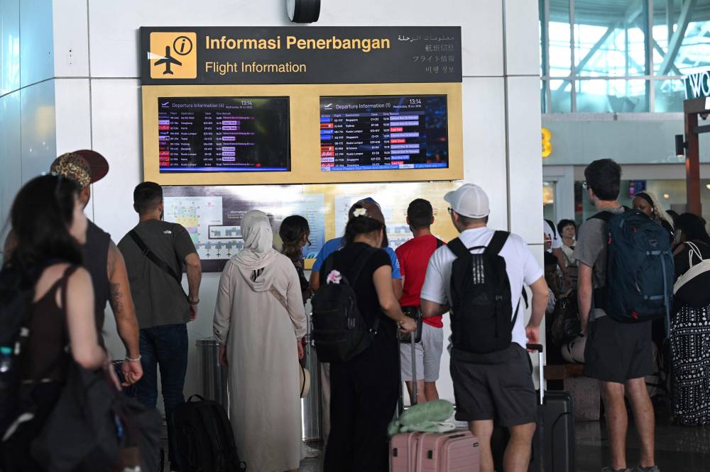 Passengers look at electronic boards displaying cancelled flights after the nearby Mount Lewotobi Laki-Laki volcano catapulted an ash tower miles into the sky, at the Ngurah Rai International Airport in Tuban near Denpasar. Photo by Sonny Tumbelaka/AFP