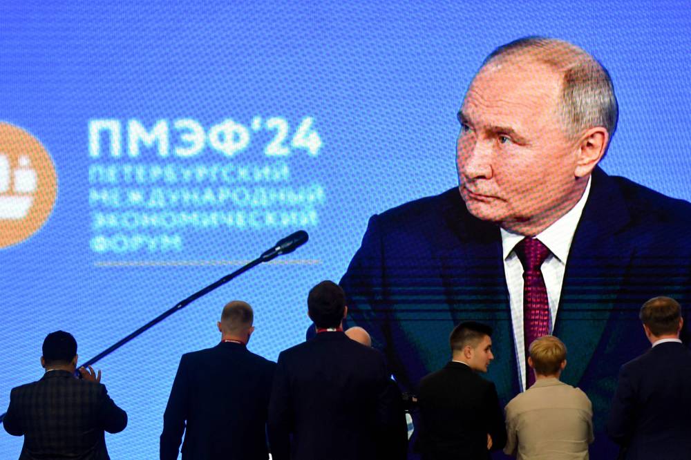 Participants stand next to a giant screen broadcasting Russia's President Vladimir Putin's address during the Saint Petersburg International Economic Forum (SPIEF) in Saint Petersburg on June 7, 2024. Westerners are set to be few and far between at Vladimir Putin's landmark business forum, once an emblem of East-West ties, which kicks off on June 18, 2025 in the Russian president's home city of Saint Petersburg. (Photo by Olga MALTSEVA / AFP)