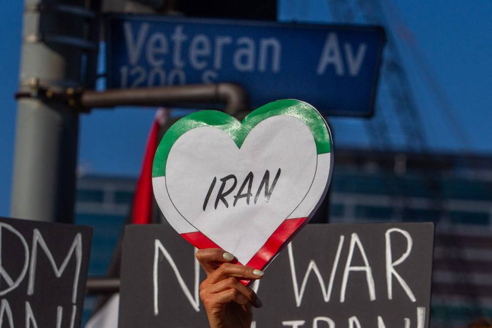 A woman holds a heart shaped sign in the colors of the Iranian flag as protesters rally during a 